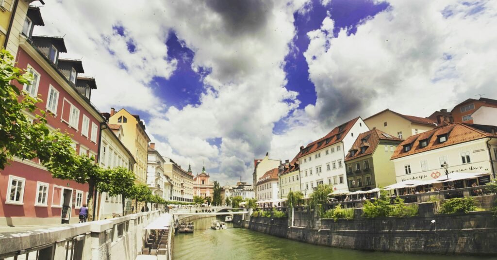 Scenic view of colorful riverside buildings in Ljubljana, showcasing vibrant architecture under dramatic skies.
