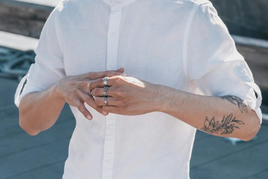 Close-up of a person's tattooed hands wearing rings against an outdoor background.
