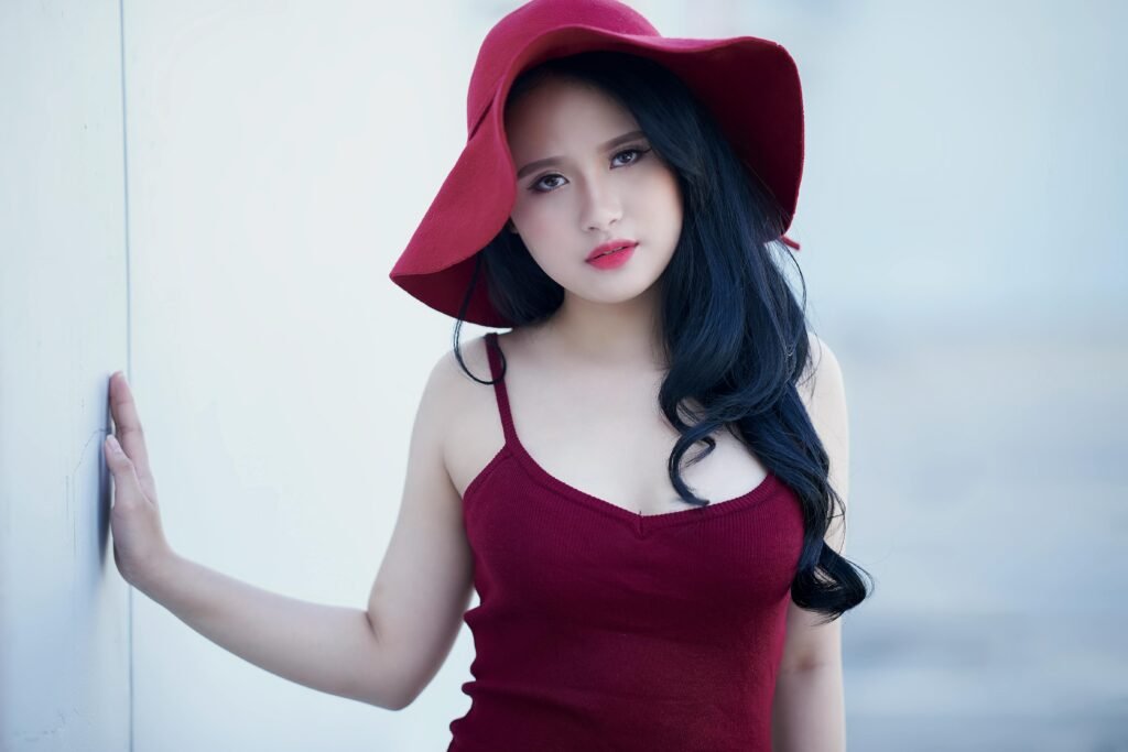 Stylish woman in a red hat and dress posing outdoors, exuding elegance and charm.